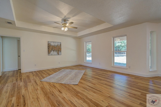 empty room featuring ceiling fan, light hardwood / wood-style flooring, a textured ceiling, and a tray ceiling