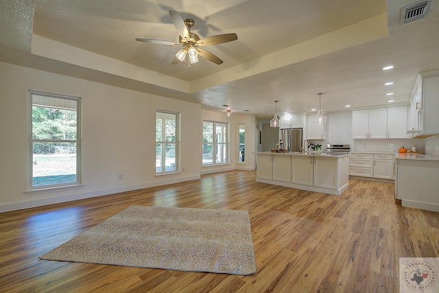 kitchen with decorative light fixtures, white cabinetry, a tray ceiling, and a center island with sink