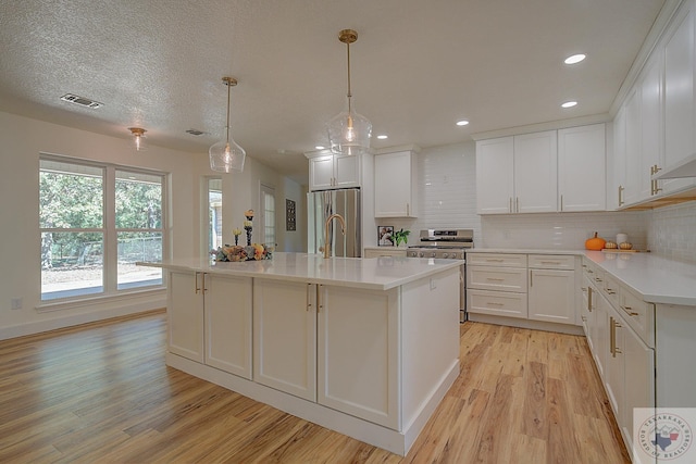 kitchen featuring appliances with stainless steel finishes, white cabinetry, light hardwood / wood-style flooring, backsplash, and an island with sink