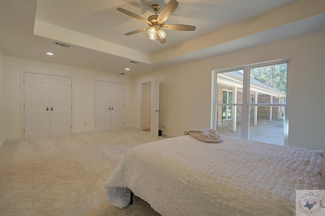 bedroom with ceiling fan, multiple closets, carpet flooring, and a tray ceiling