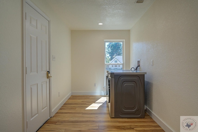 laundry room with washer / dryer, light hardwood / wood-style floors, and a textured ceiling