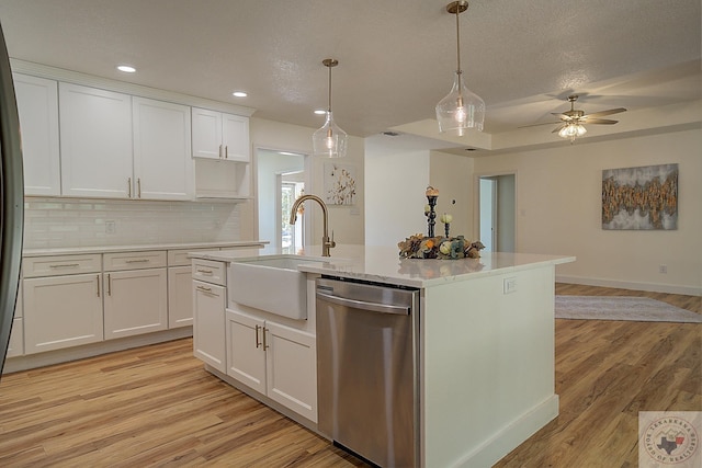 kitchen featuring stainless steel dishwasher, sink, backsplash, white cabinets, and a center island with sink