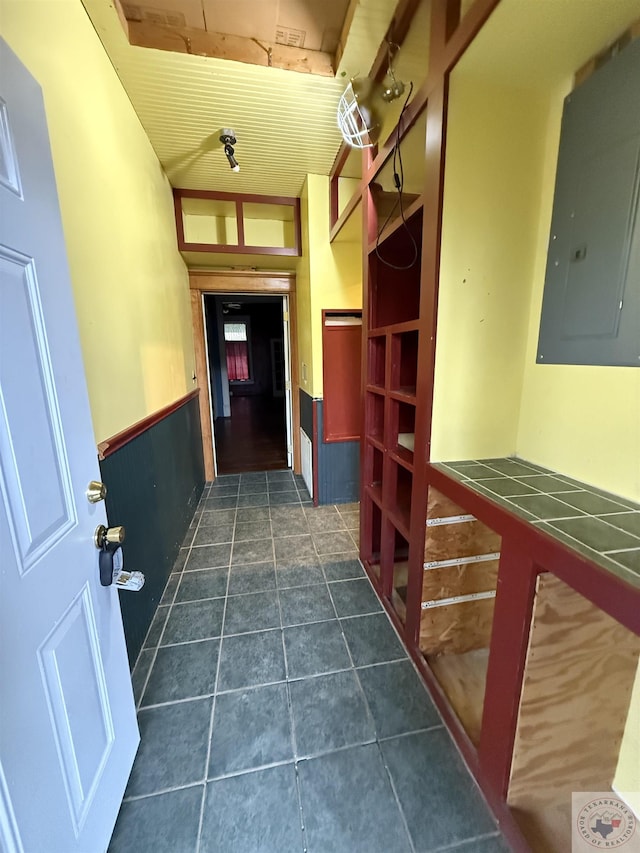 corridor with dark tile patterned flooring, electric panel, and wainscoting