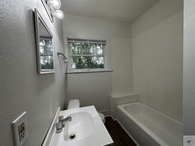 bathroom with a textured ceiling, vanity, a tub to relax in, toilet, and hardwood / wood-style flooring