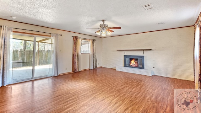 unfurnished living room featuring hardwood / wood-style floors, a textured ceiling, ceiling fan, a brick fireplace, and crown molding