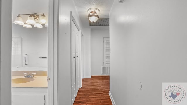 hallway with dark wood-type flooring, sink, and a textured ceiling