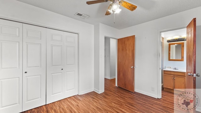 unfurnished bedroom featuring ensuite bathroom, a textured ceiling, wood-type flooring, a closet, and ceiling fan