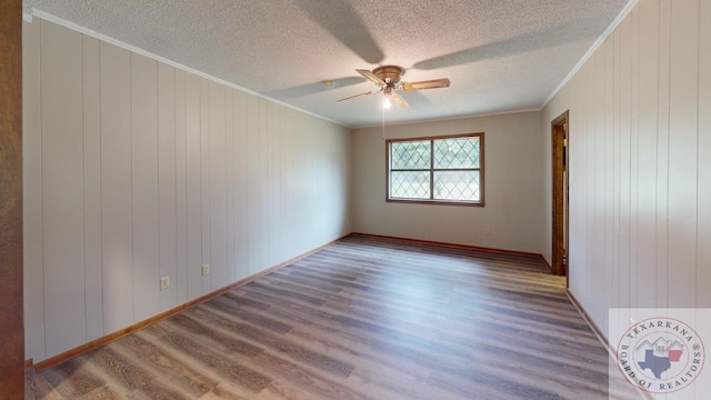 unfurnished room featuring a textured ceiling, hardwood / wood-style flooring, ornamental molding, ceiling fan, and wood walls