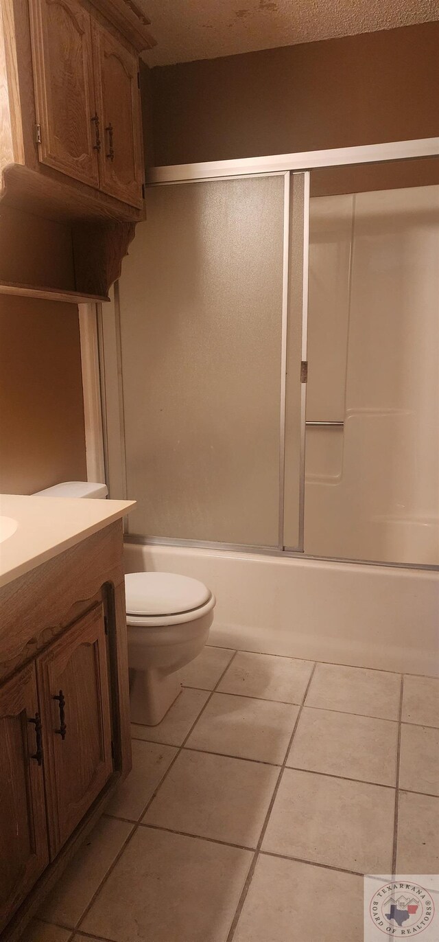 full bathroom with combined bath / shower with glass door, toilet, tile patterned flooring, and vanity