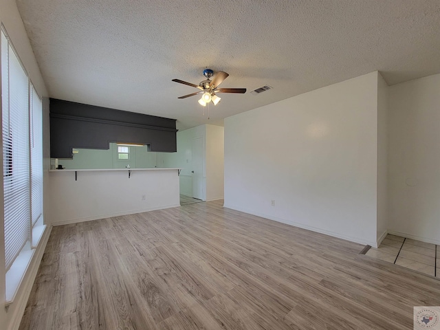 unfurnished living room with ceiling fan, light hardwood / wood-style floors, and a textured ceiling