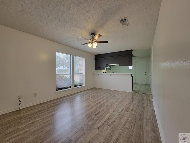 unfurnished living room with wood-type flooring, a textured ceiling, and ceiling fan