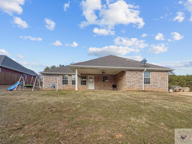 back of house with a playground, brick siding, fence, a ceiling fan, and a yard