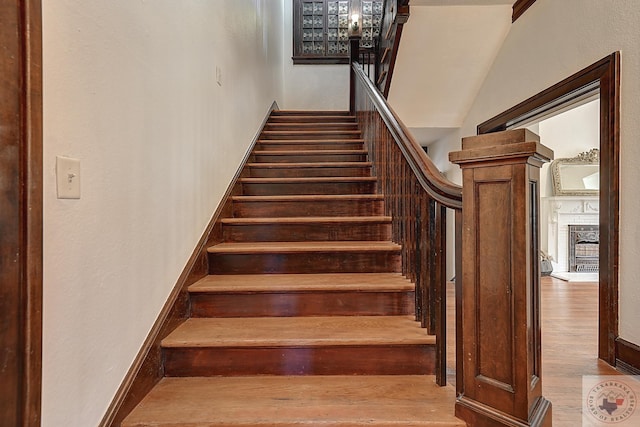 stairs with a fireplace with raised hearth and wood finished floors