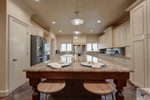 kitchen with light stone countertops, stainless steel fridge, a kitchen island, and pendant lighting