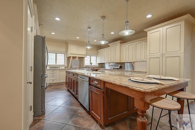 kitchen with a textured ceiling, light stone counters, hanging light fixtures, appliances with stainless steel finishes, and a center island