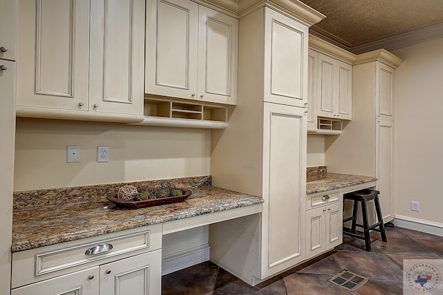 kitchen with a textured ceiling, dark stone counters, crown molding, and built in study area