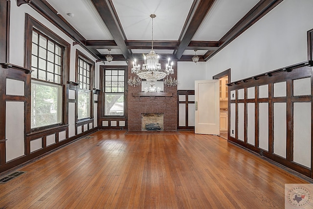 unfurnished living room with visible vents, coffered ceiling, wood finished floors, an inviting chandelier, and a brick fireplace