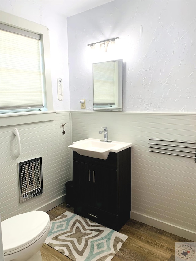 bathroom with wood-type flooring, toilet, heating unit, and vanity