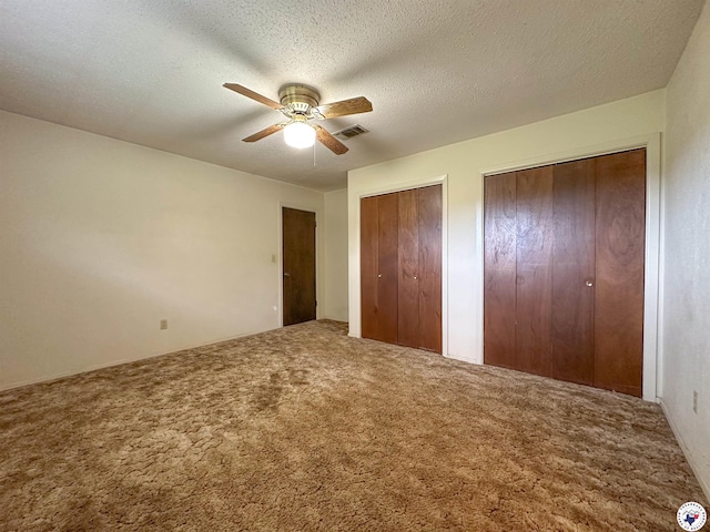 unfurnished bedroom with carpet floors, visible vents, two closets, and ceiling fan