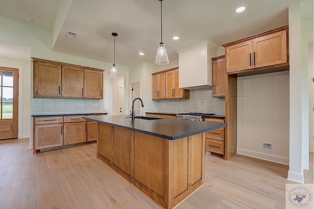 kitchen with sink, an island with sink, hanging light fixtures, and light hardwood / wood-style flooring