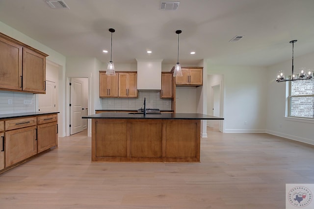 kitchen with sink, an island with sink, hanging light fixtures, and light hardwood / wood-style floors