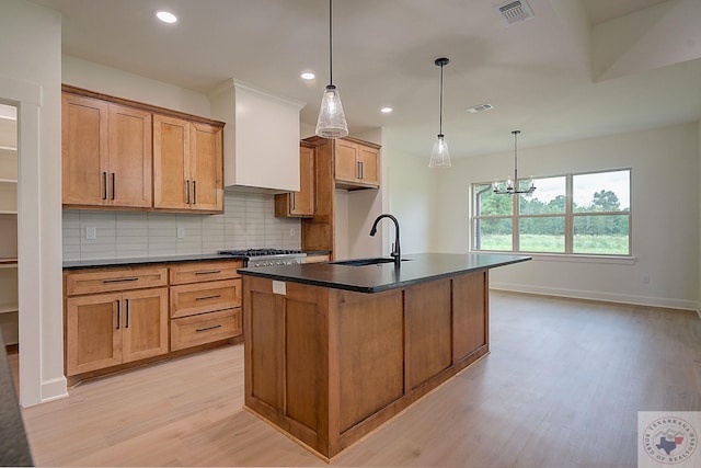 kitchen with light hardwood / wood-style flooring, pendant lighting, sink, backsplash, and a kitchen island with sink