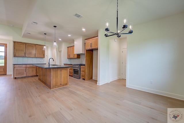 kitchen featuring decorative light fixtures, backsplash, high end stainless steel range oven, a kitchen island with sink, and light hardwood / wood-style floors