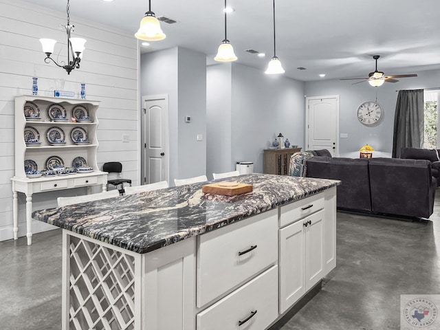 kitchen with white cabinets, a center island, decorative light fixtures, dark stone countertops, and wood walls