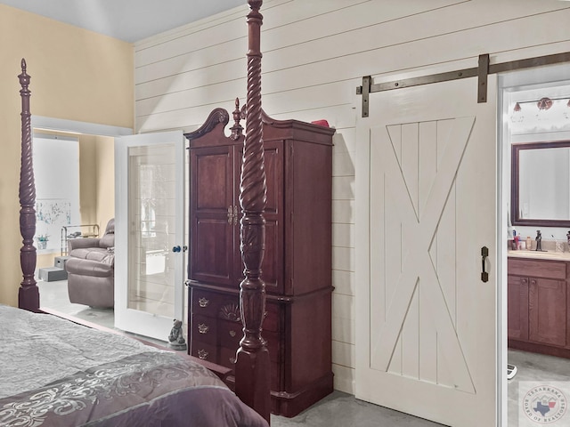 bedroom featuring sink, wood walls, connected bathroom, and a barn door