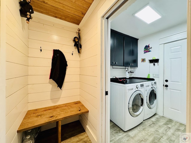 laundry area with washing machine and dryer, wood walls, light wood-style flooring, wooden ceiling, and cabinet space