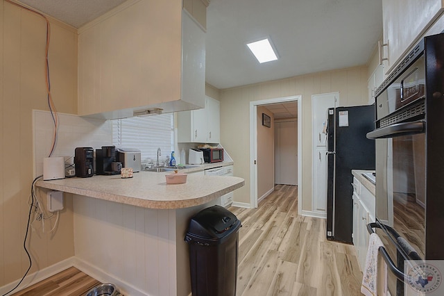 kitchen with white cabinets, black oven, sink, kitchen peninsula, and light wood-type flooring