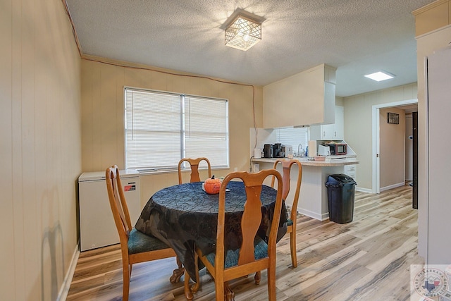 dining room featuring wood walls, light wood-type flooring, and a textured ceiling