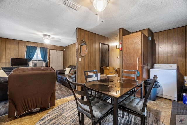 dining space with a textured ceiling, washer / clothes dryer, wooden walls, and ceiling fan