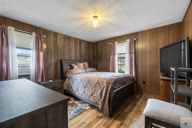 bedroom with wood walls, light wood-type flooring, and a textured ceiling