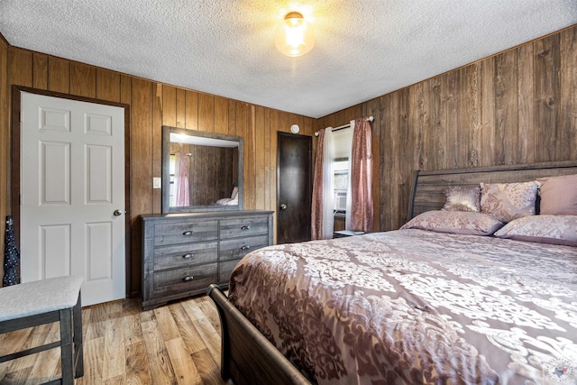 bedroom featuring light wood-type flooring, wooden walls, and a textured ceiling