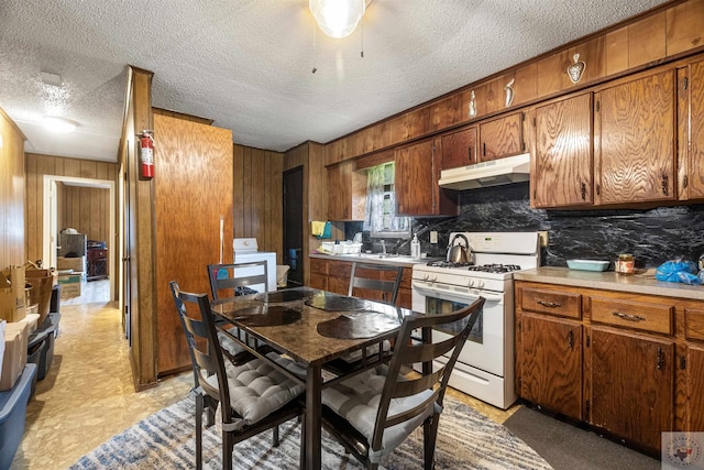 kitchen with a textured ceiling, white gas stove, washer / dryer, and wood walls