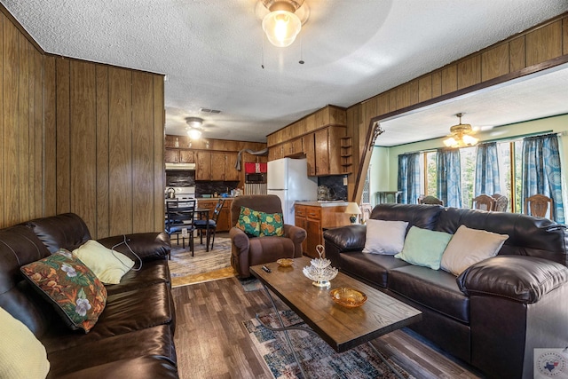 living room with wooden walls, a textured ceiling, dark hardwood / wood-style floors, and ceiling fan