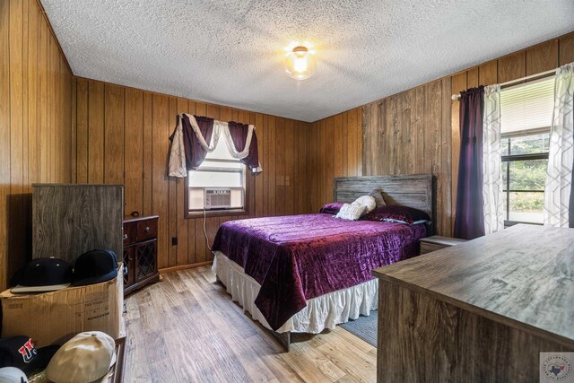 bedroom featuring a textured ceiling, light hardwood / wood-style floors, wooden walls, and cooling unit