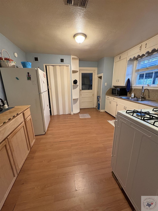 kitchen featuring visible vents, freestanding refrigerator, a sink, stove, and light wood-type flooring