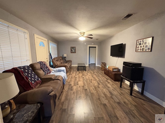 living room featuring visible vents, ceiling fan, baseboards, wood finished floors, and a textured ceiling