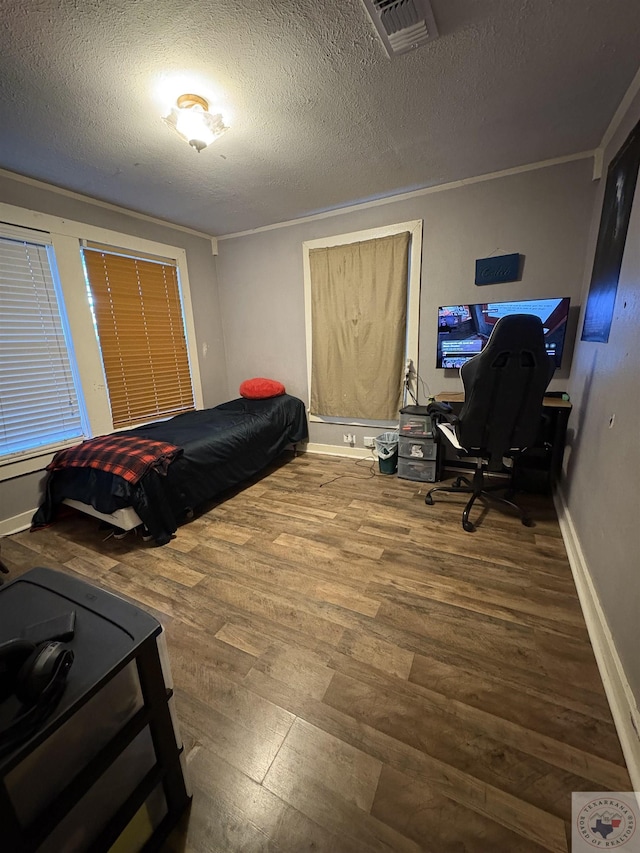 bedroom featuring wood finished floors, baseboards, visible vents, ornamental molding, and a textured ceiling