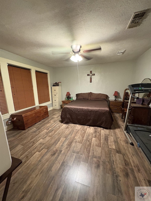 bedroom featuring a ceiling fan, wood finished floors, visible vents, and a textured ceiling