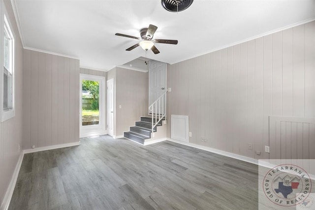 unfurnished living room with wood-type flooring, wood walls, ceiling fan, and ornamental molding