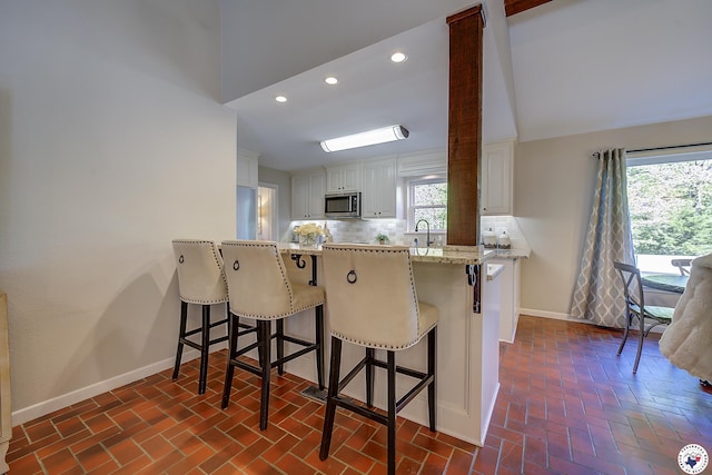986 Texas Highway 77 W, Atlanta, TX 75551 - kitchen with white cabinets, baseboards, a sink, stainless steel microwave, and brick floor