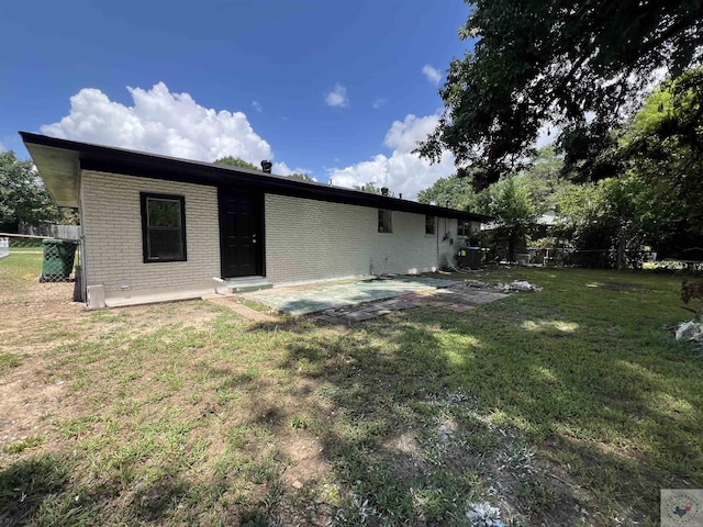 rear view of house with brick siding, a yard, and fence