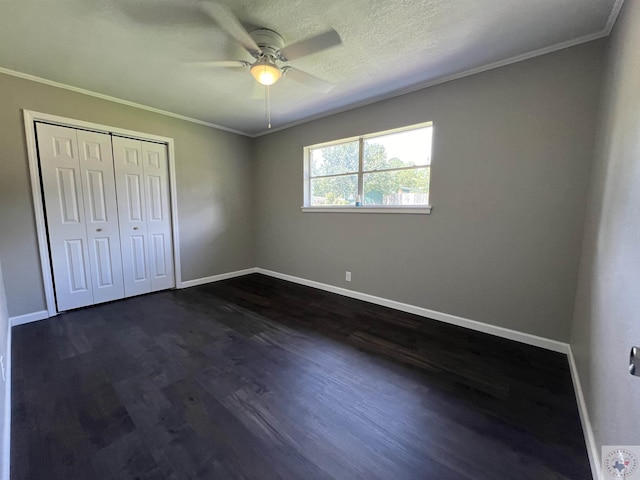 unfurnished bedroom featuring a textured ceiling, dark wood-type flooring, a closet, ornamental molding, and ceiling fan