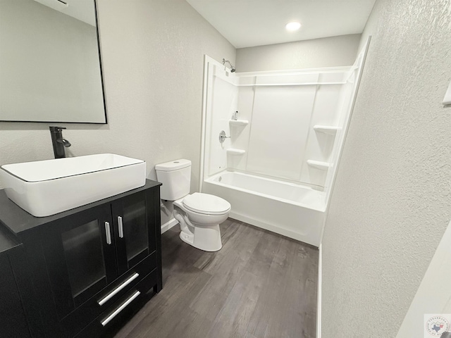 bathroom with a textured wall, toilet, wood finished floors, vanity, and shower / bathing tub combination