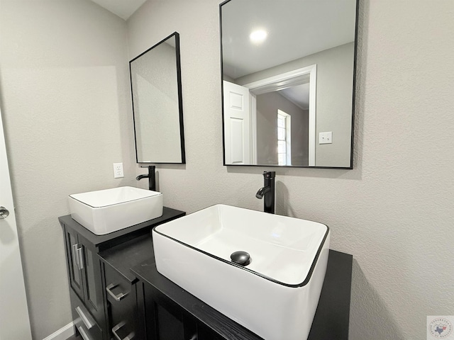 bathroom with double vanity, a sink, and a textured wall