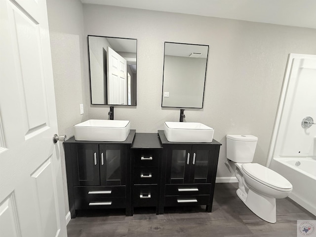 full bath with double vanity, wood finished floors, a sink, and toilet