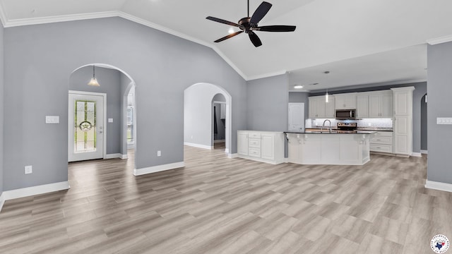 unfurnished living room with a sink, arched walkways, light wood-type flooring, baseboards, and ceiling fan